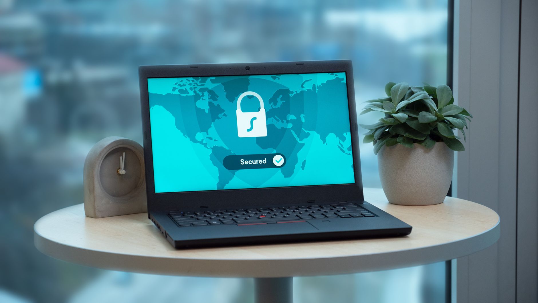 Laptop z ikoną kłódki na ekranie na biurku obok zegara i rośliny