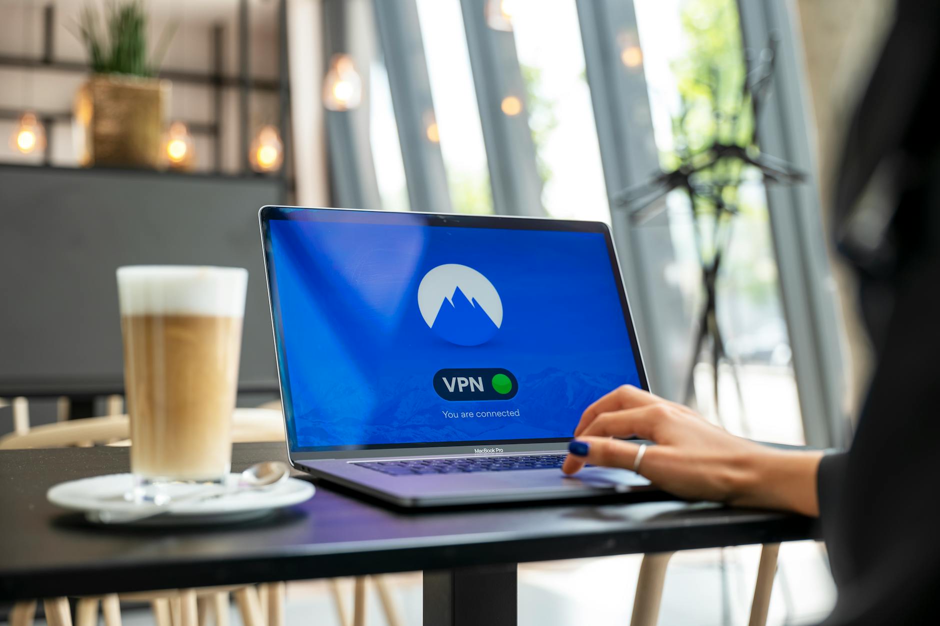 10 praktycznych zasad bezpieczeństwa danych w chmurze dla freelancerów i mikrofirm Osoba pracująca zdalnie w kawiarni na laptopie z włączonym VPN