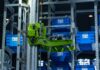 Sztuczna inteligencja w logistyce produkcji: mniej przestojów, niższe koszty Zielone ramię robota w zautomatyzowanym magazynie przenosi niebieskie skrzynki