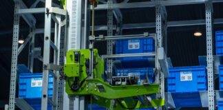 Zielone ramię robota w zautomatyzowanym magazynie przenosi niebieskie skrzynki