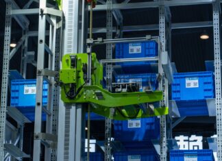 Zielone ramię robota w zautomatyzowanym magazynie przenosi niebieskie skrzynki
