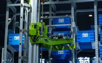 Sztuczna inteligencja w logistyce produkcji: mniej przestojów, niższe koszty Zielone ramię robota w zautomatyzowanym magazynie przenosi niebieskie skrzynki