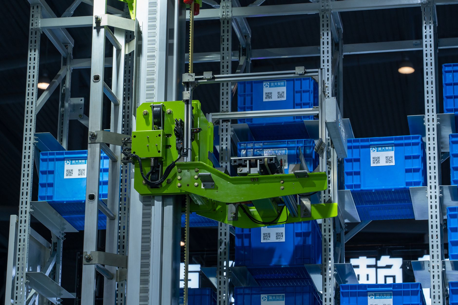 Sztuczna inteligencja w logistyce produkcji: mniej przestojów, niższe koszty Zielone ramię robota w zautomatyzowanym magazynie przenosi niebieskie skrzynki