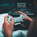 Legalność emulatorów, ROM‑ów i retro‑gier: co wolno miłośnikowi starych konsol Dłonie trzymające retro kontroler Sony z konsolą Sega Mega Drive w tle