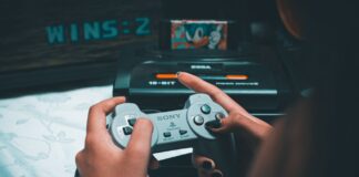 Dłonie trzymające retro kontroler Sony z konsolą Sega Mega Drive w tle