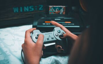 Dłonie trzymające retro kontroler Sony z konsolą Sega Mega Drive w tle