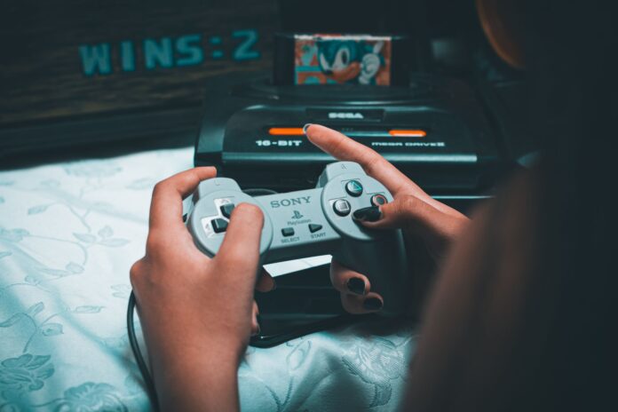 Dłonie trzymające retro kontroler Sony z konsolą Sega Mega Drive w tle Dłonie trzymające retro kontroler Sony z konsolą Sega Mega Drive w tle