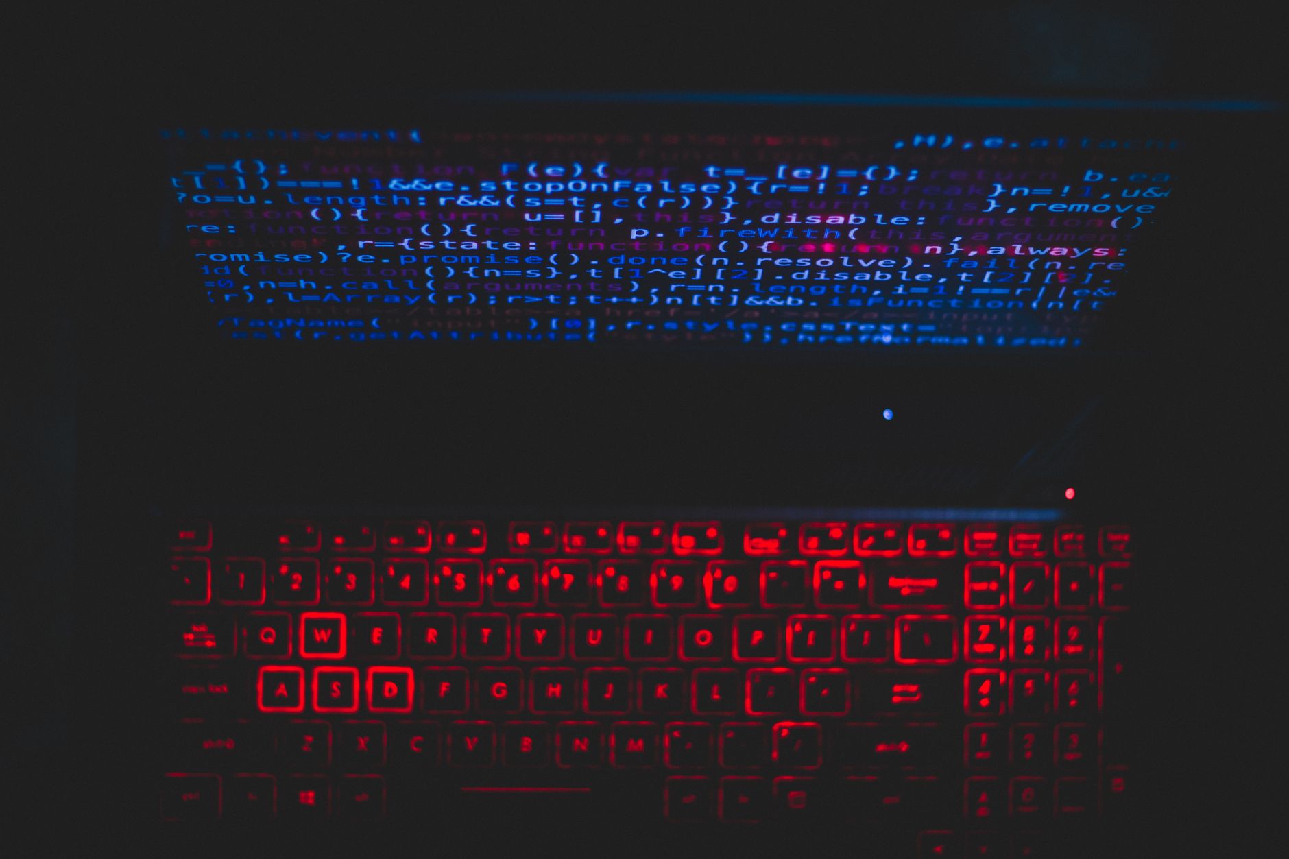 Laptop z ciemnym motywem, czerwono podświetloną klawiaturą i kodem na ekranie